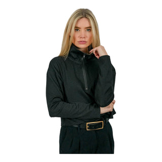 A woman with blonde hair and a contemplative expression poses with her hand on her chin, wearing a zipped-up black EMF protective jacket, showcasing its sleek design and functionality for shielding against electromagnetic fields.