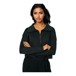 A woman with a confident stance and dark hair gazes forward, arms folded, sporting a partially zipped black EMF protective jacket that combines a modern look with functionality for electromagnetic field shielding.