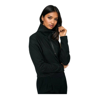 A woman with sleek dark hair and a gentle gaze holds her chin thoughtfully, clad in a high-necked black EMF protective jacket, her arms crossed in a relaxed pose that underscores the jacket's combination of style and electromagnetic field protection.