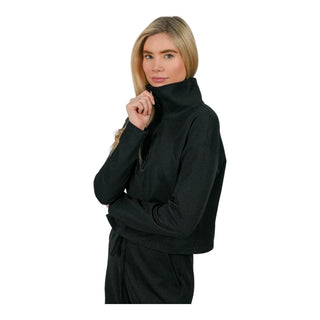 A poised woman with flowing blonde hair models a black EMF protective turtleneck with a contemplative gaze, her hand gently touching her chin, emphasizing the garment's cozy elegance and its purpose to shield from electromagnetic fields.