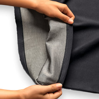 A person's hands revealing the inner silver lining of a piece of black EMF shielding apparel, demonstrating the garment's protective layer designed to block electromagnetic fields for the wearer